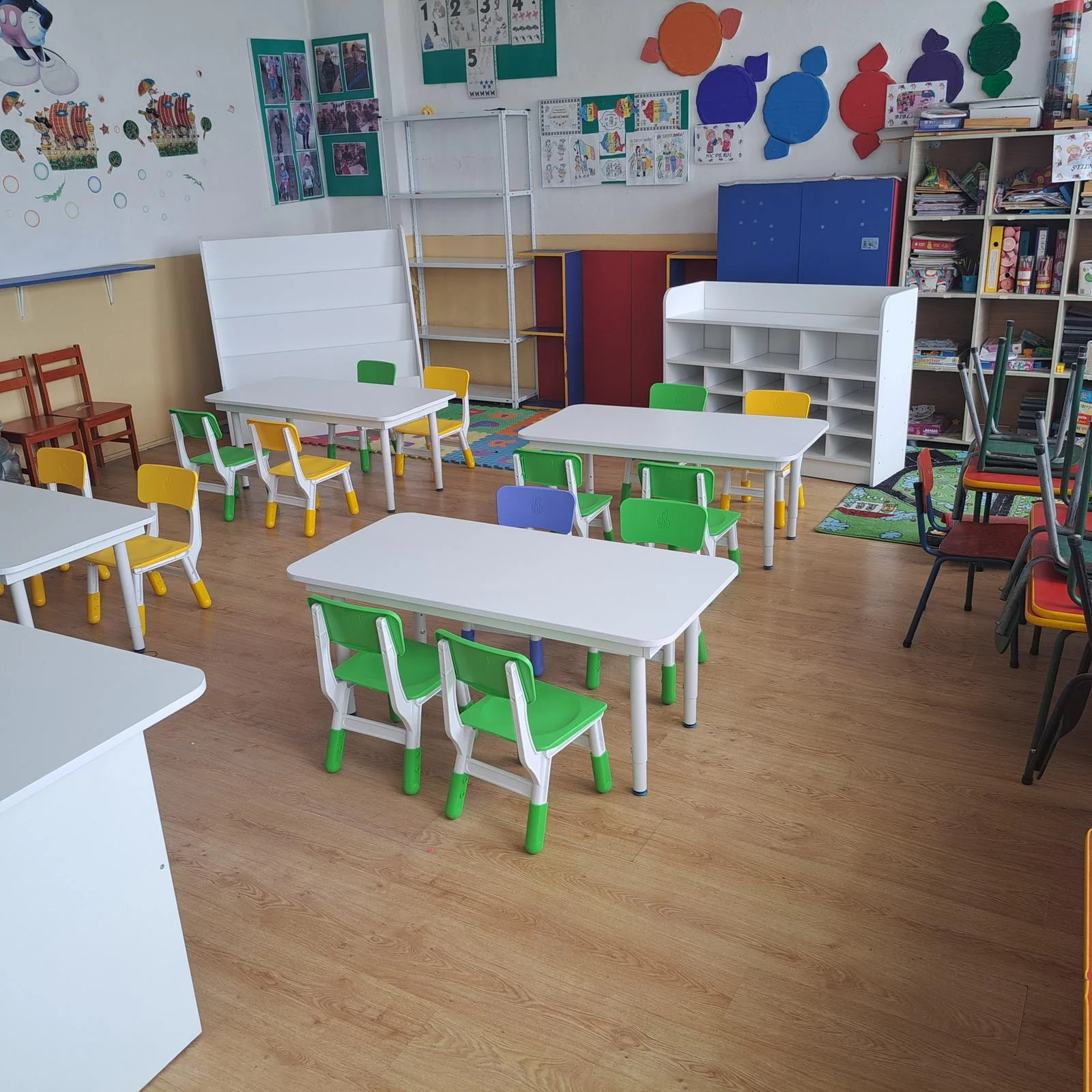 Sala gradinita mese albe scaune verzi rafturi biblioteca